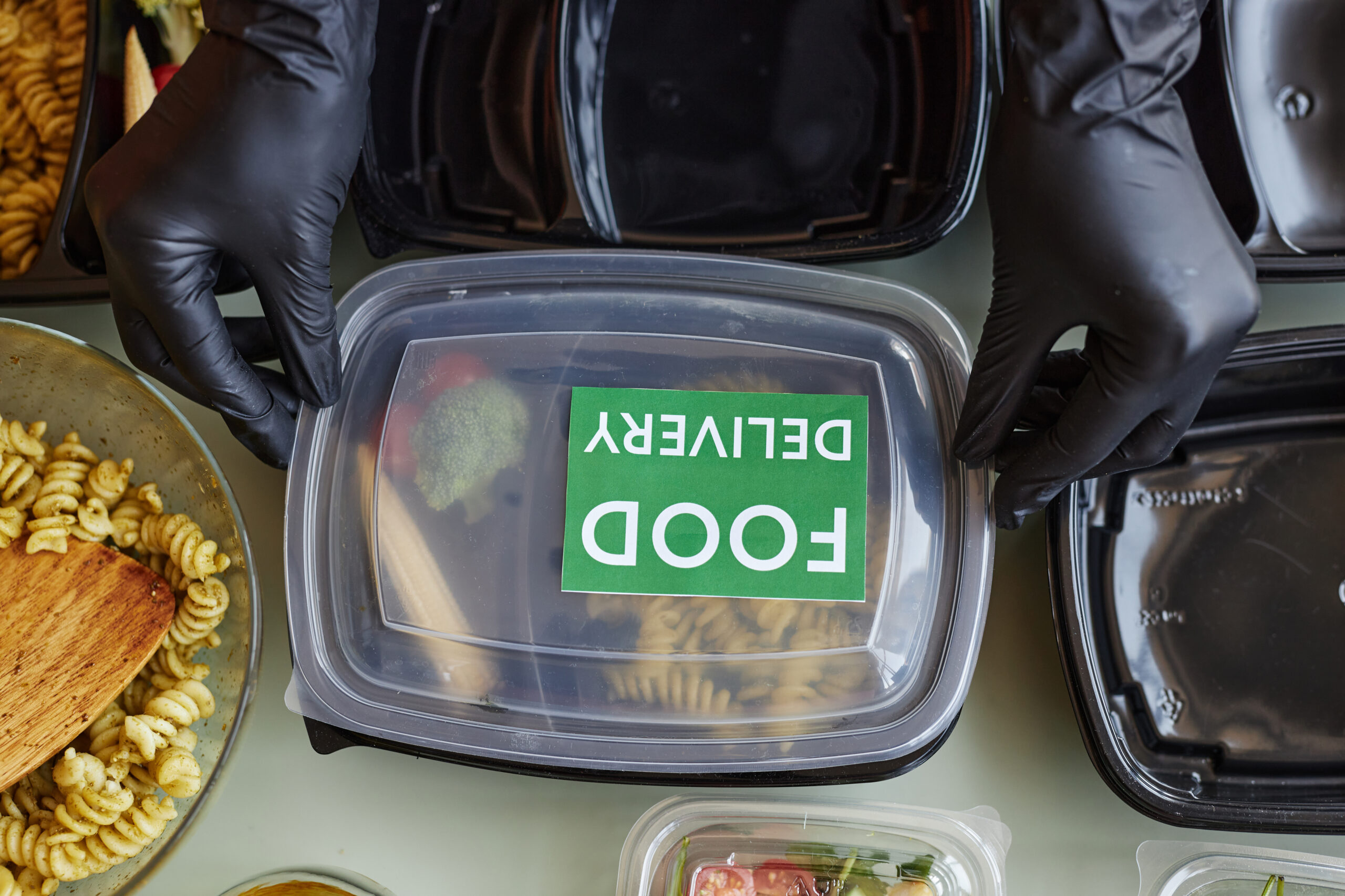 Top view cafe worker closing plastic container with Food delivery sticker Cateraars