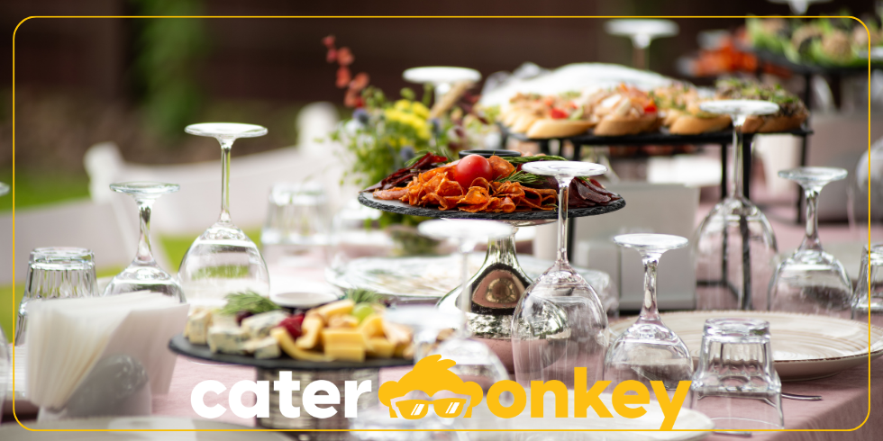 Mesa de catering montada com travessas de comida e copos de vinho ao ar livre