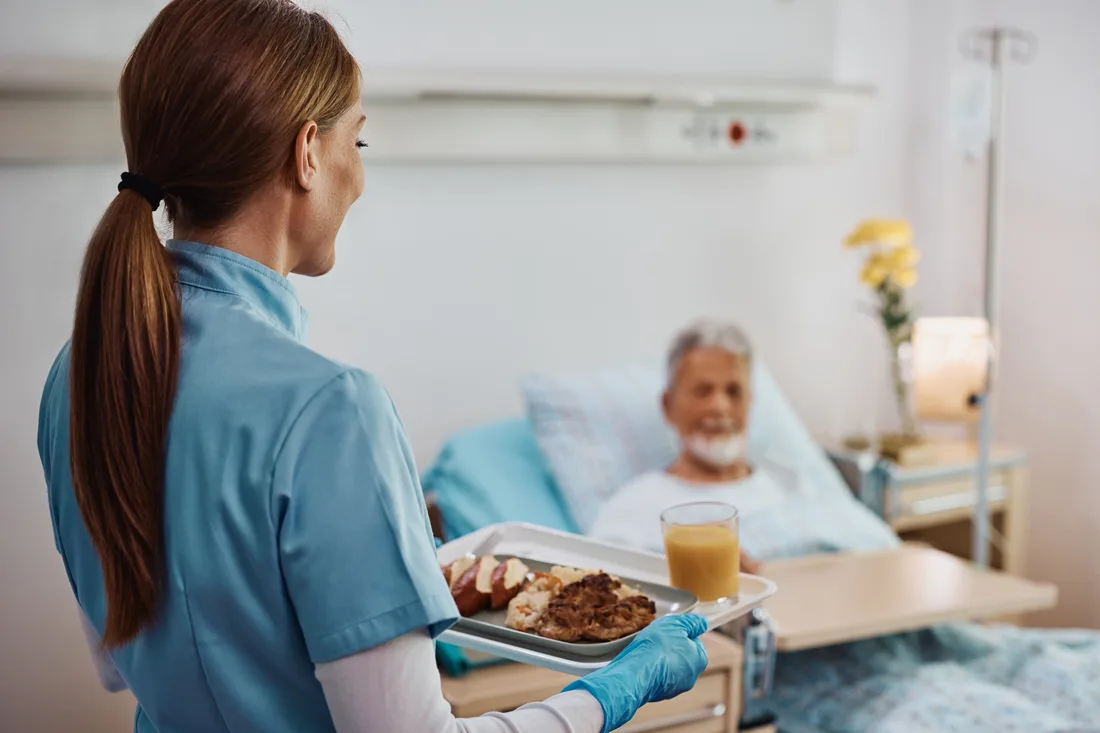 Verpleegkundige brengt een maaltijd naar een patiënt