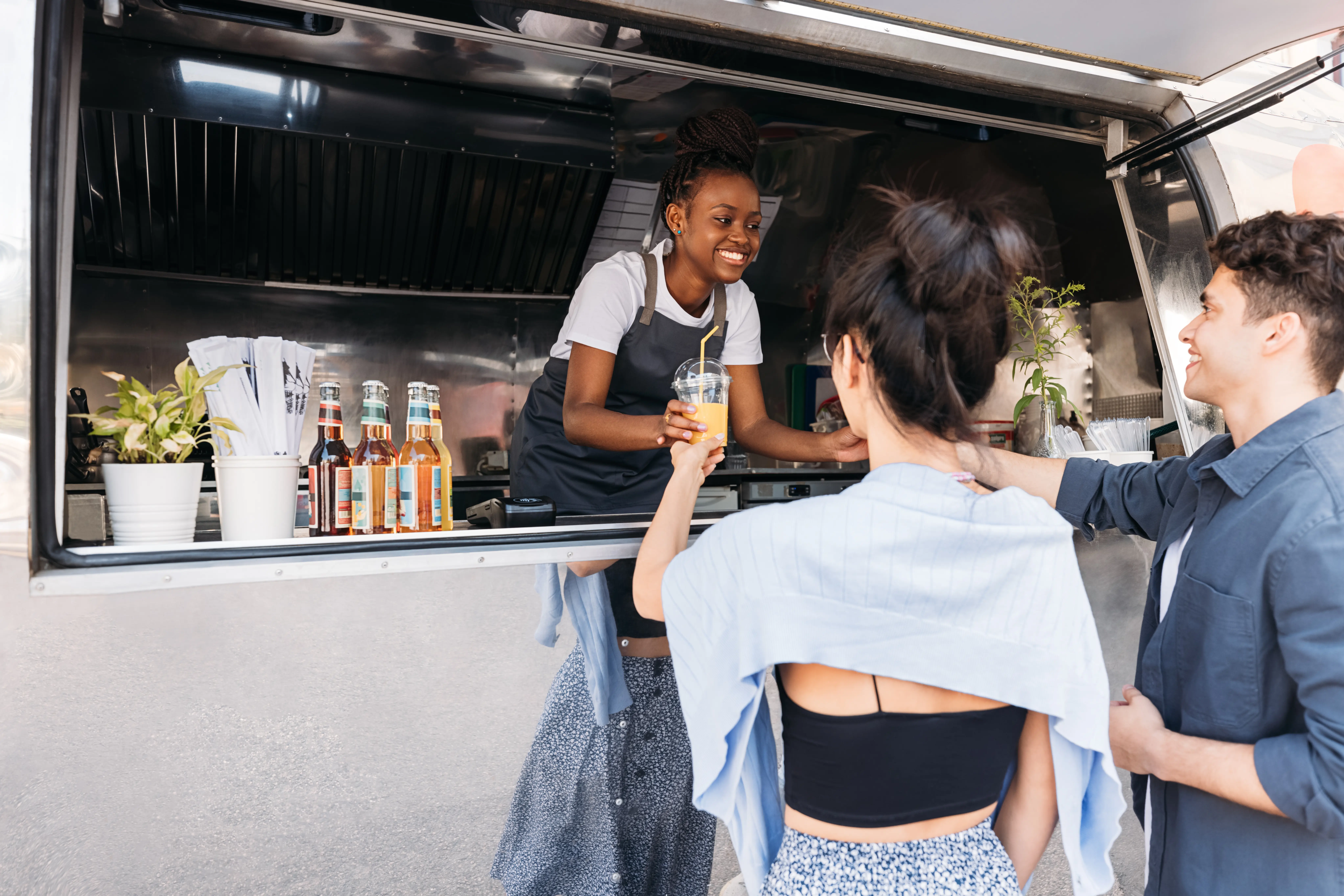 Male and female friends receiving drinks from smiling food truck owner in the city Company vs Festival