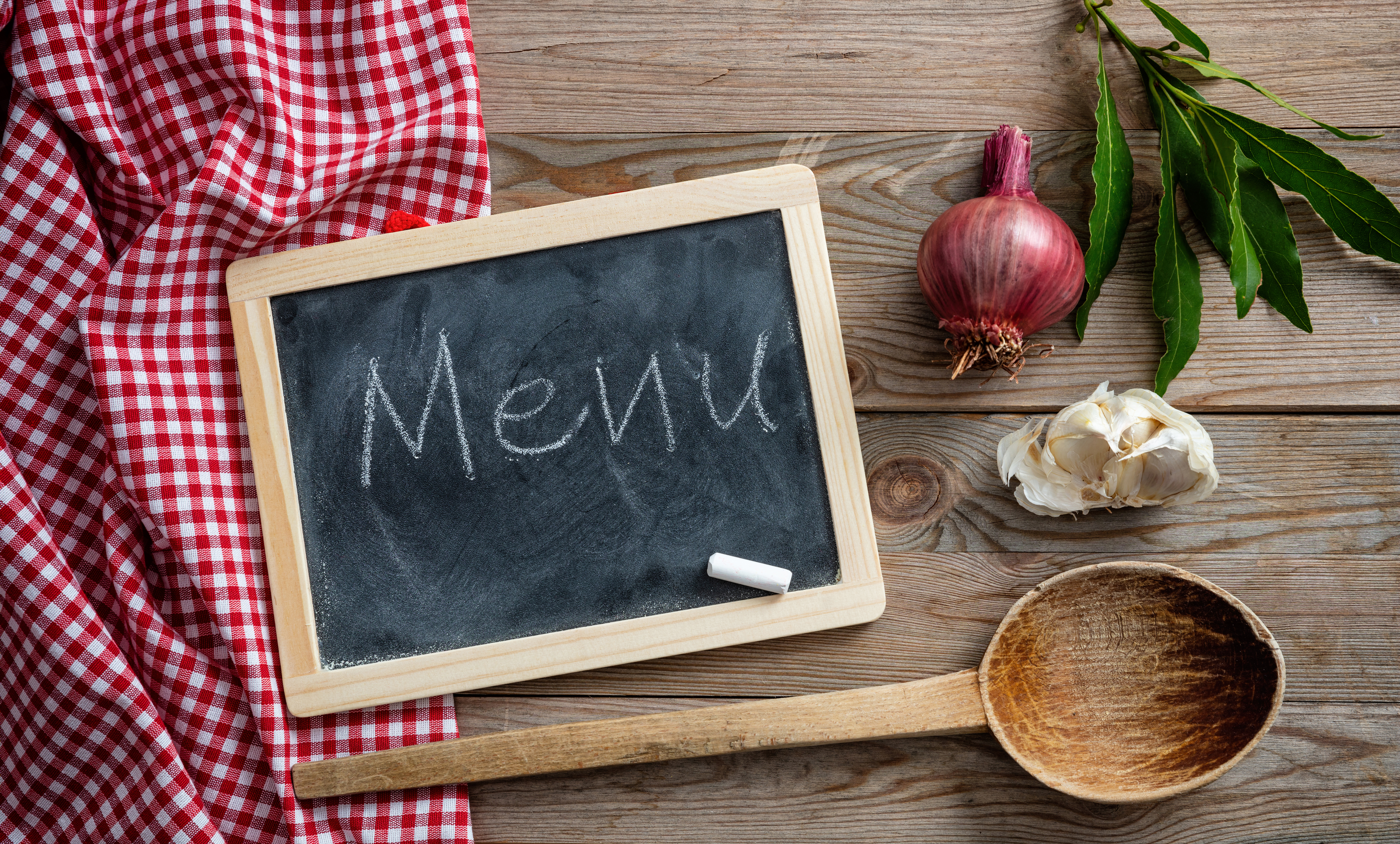 Menu text on a blackboard, herbs and a ladle on red tablecloth and wooden table, top view Cateraars